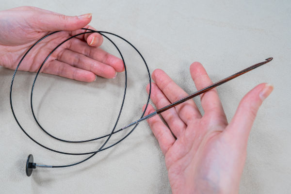 Une personne tient une aiguille à tricoter circulaire avec un long câble flexible reliant deux pointes d'aiguille, dont l'une est montrée de près, ressemblant aux outils utilisés pour le crochet tunisien.