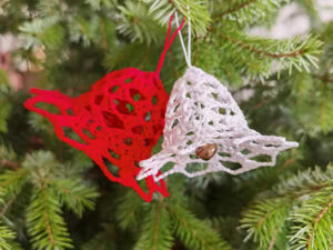 Deux clochettes crochetées, l'une rouge et l'autre blanche, sont suspendues aux branches d'un pin vert - un modèle crochet de Noël facile parfait pour un décor de vacances festif.