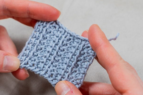 Une personne tenant un morceau de fil, s'apprêtant à créer des motifs délicats en utilisant la technique du point tunisien au crochet.