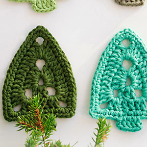 Deux arbres crochetés, l'un vert foncé et l'autre vert clair, sont présentés sur une surface blanche avec de petites branches vertes au premier plan.