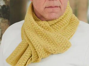 Un homme portant une écharpe homme au crochet jaune clair enroulée autour de son cou, associée à une chemise blanche. L'arrière-plan est légèrement flou, suggérant un environnement extérieur.