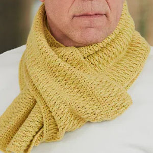 Une personne portant une épaisse écharpe jaune tricotée autour du cou, avec un gros plan sur l'écharpe homme au crochet et la partie inférieure du visage.