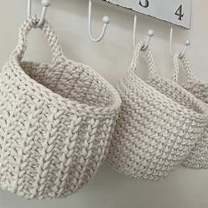 Trois paniers crochetés à la main de couleur crème sont suspendus à des crochets blancs sur un support mural avec des numéros visibles, présentant une poignée solide et un motif texturé - parfait pour ceux qui recherchent une explication gratuite de panier au crochet.