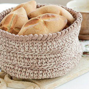 Un panier rond, tressé selon une technique inspirée d'une explication gratuite de panier au crochet, repose sur une surface en bois, rempli de petits pains fraîchement cuits à la croûte dorée et croustillante.