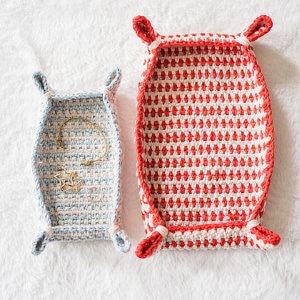 Deux plateaux crochetés, l'un petit et bleu avec des bijoux à l'intérieur, l'autre plus grand et rouge, sont posés côte à côte sur une surface blanche. Tous deux présentent quatre coins en boucle, parfaits pour exposer les trouvailles après avoir suivi une explication gratuite de panier au crochet.