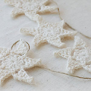 Des étoiles blanches au crochet, inspirées d'un modèle d'étoile au crochet gratuit, sont reliées par une fine ficelle et disposées sur un fond de tissu clair.