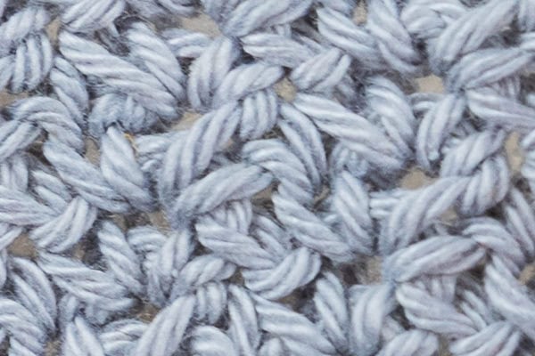 Gros plan d'un fil bleu clair crocheté selon un motif texturé de ramage au crochet à points imbriqués, montrant les brins individuels et les boucles des points.