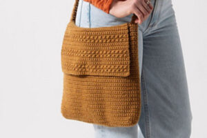 Une personne portant un jean bleu clair et un haut orange tient un sac bandoulière au crochet jaune moutarde avec une fermeture à rabat élégante.