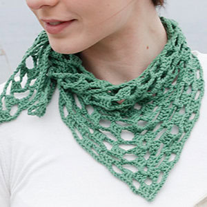 Une personne porte un foulard vert clair, en dentelles, crocheté à la main et noué autour de son cou avec un haut blanc uni. Le motif ouvert et aéré du foulard est parfait pour tous ceux qui recherchent un tuto de châle au crochet facile.