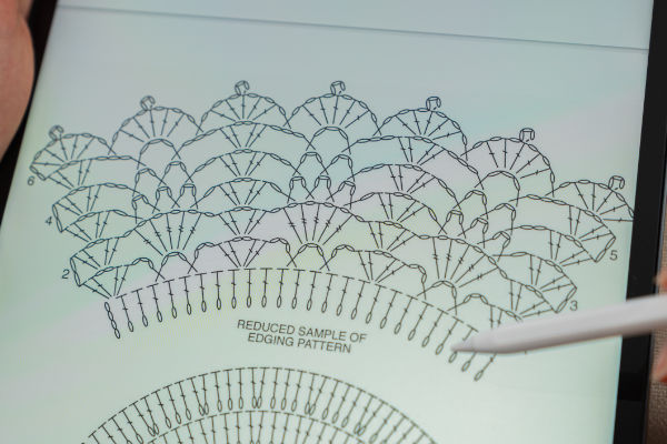 Gros plan sur l'écran d'une tablette affichant des schémas de motifs de bordures au crochet, avec un stylet pointant vers la section intitulée « Exemple réduit de motif de bordure ».