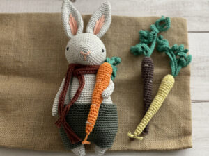 Un doudou lapin au crochet tenant une carotte, entouré de carottes ludiques.