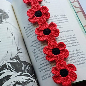 Un marque-page crocheté rouge avec cinq fleurs, chacune avec un centre noir, se trouve sur les pages ouvertes d'un livre avec un texte en français et une illustration en noir et blanc.