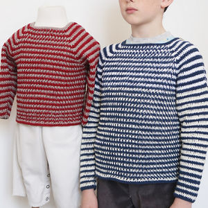 Un enfant portant un pull à rayures bleues et blanches se tient à côté d'un mannequin vêtu d'un pull similaire à rayures rouges et blanches et d'un pantalon blanc.