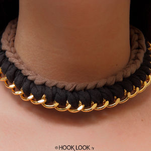 Gros plan sur le cou d'une personne portant un collier ras-de-cou en tissu tressé marron et noir, avec des chaînes dorées sur le bord inférieur.