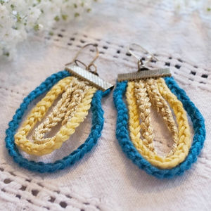 Boucles d'oreilles au crochet avec une boucle intérieure jaune et une boucle extérieure bleue, attachées à des crochets en argent, présentées sur un fond de tissu texturé clair.