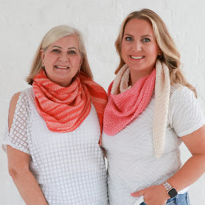 Deux femmes souriantes et proches l'une de l'autre, toutes deux vêtues d'un haut blanc et d'un foulard à motifs roses, sur un fond blanc uni.