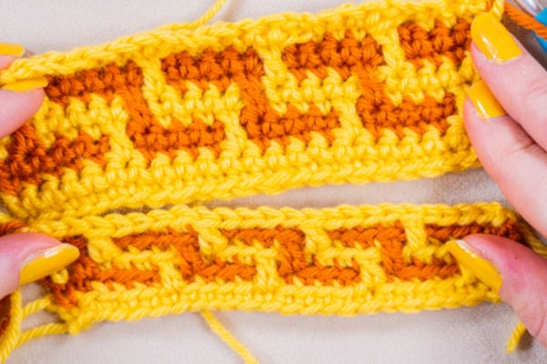 Deux mains aux ongles peints en jaune tiennent des échantillons au crochet présentant un motif géométrique de « mosaïque au crochet » réalisé avec des fils jaune vif et orange. Les motifs en mosaïque ou entrelacés sont mis en valeur sur un fond clair.