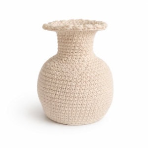 Un vase rond, de couleur beige, au bord large et évasé, entièrement recouvert d'un motif texturé tricoté ou crocheté.