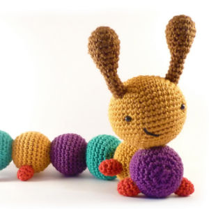 Une chenille en crochet avec une tête jaune, des antennes marron, des pattes rouges et un corps composé de segments ronds colorés en bleu, violet et jaune.