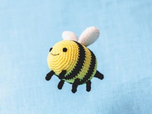 Une ravissante abeille au crochet, ornée de rayures jaunes et noires éclatantes, d'ailes blanches délicates et d'un visage souriant et joyeux, se détache sur un fond bleu clair.