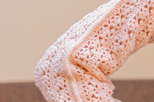 Gros plan sur une couverture de bébé rose au crochet, mettant en valeur son motif « couture au crochet » très travaillé et sa texture douce, drapée avec élégance sur une surface.