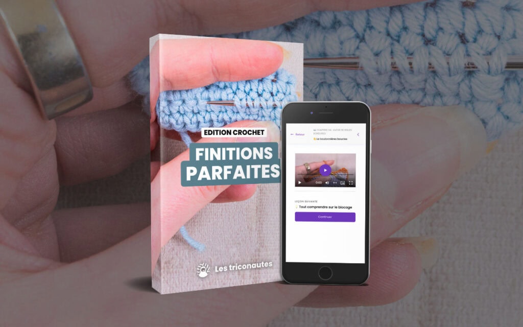 Gros plan sur des mains en train de crocheter avec du fil bleu, avec en arrière-plan un livre intitulé « Edition Crochet : Finitions Parfaites » et un smartphone sur lequel est affichée une vidéo tutoriel de crochet.