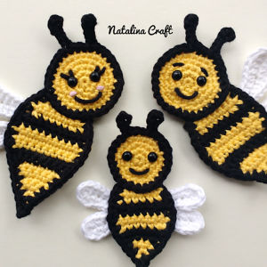 Trois abeilles au crochet, rayées de noir et de jaune, dotées d'antennes noires et d'ailes blanches, sont représentées sur un fond blanc. L'une d'elles a les joues roses. L'inscription « Natalina Craft » figure en haut de l'image.