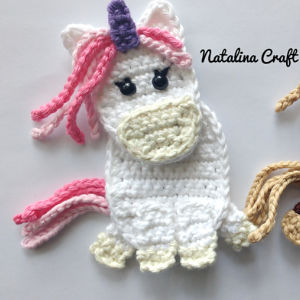 Une licorne blanche au crochet, avec une crinière rose, une corne violette, des yeux noirs, un museau couleur crème et des sabots, représentée sur un fond blanc. L'inscription « Natalina Craft » apparaît dans le coin supérieur droit.