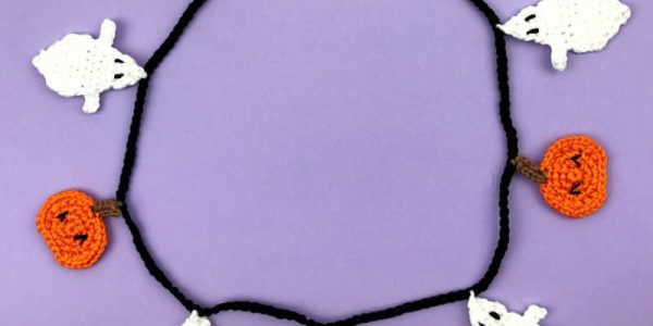 Une guirlande d'Halloween réalisée au crochet : d'adorables fantômes blancs et des citrouilles orange, tous crochetés, disposés en cercle sur un fond violet.