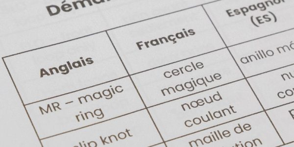 Gros plan sur un tableau multilingue de termes de crochet anglais-français, présentant des termes de crochet en anglais, en français tels que « magic ring » / « cercle magique » » et « slip knot » / « nœud coulant »