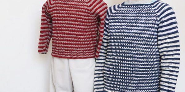 Un enfant portant un pull à rayures bleues et blanches, fabriqué à partir d'un tuto pull au crochet pour garcon, se tient à côté d'un mannequin vêtu d'un pull à rayures rouges et blanches et d'un pantalon blanc sur un fond blanc uni.